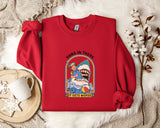 A red sweater with a graphic of a person in a blue shirt and a shark, along with the text "HANG IN THERE IT GETS WORSE", is displayed on a bed with a white blanket and a white mug.