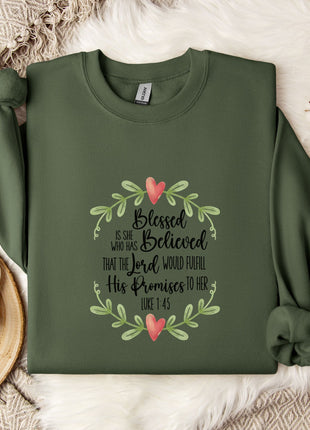 A green sweatshirt with a floral design and text printed on it, along with a mug and some white flowers on a bed.