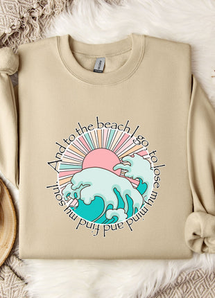 A beige sweatshirt with a graphic design depicting a beach scene, along with a mug, a branch of cotton bolls, and a snowflake.