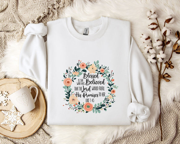 A white sweatshirt with a floral design and text printed on it, placed on a bed with a white blanket and a white mug.