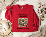 A red sweater with a cat graphic and text printed on it, along with a mug and a plant, all placed on a white surface.