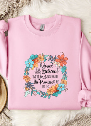 A pink sweatshirt with a floral design and text, placed on a white fur rug, along with a white mug, a wooden tray, and some white flowers.