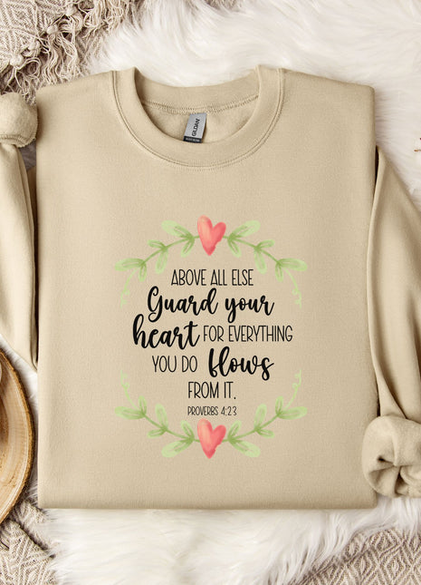 a beige sweatshirt with a printed Bible verse and a floral design, along with a mug, a white mug with a heart design, and some white flowers on a white fur-covered surface.