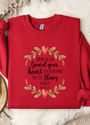 A red sweater with a printed message about guarding one's heart, along with a white mug and a branch of cotton bolls, all placed on a white fur rug.