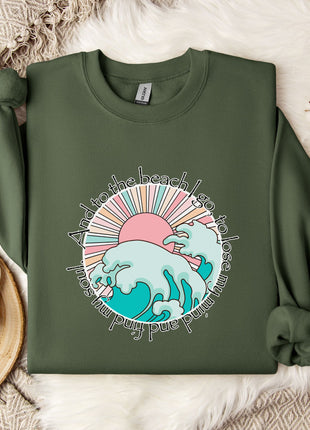 a green sweatshirt with a colorful graphic design, including a sun, waves, and text, laid out on a white surface.