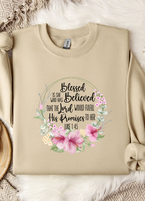 A beige sweatshirt with a floral design and text printed on it, along with a mug, a branch of cotton flowers, and a wooden tray.