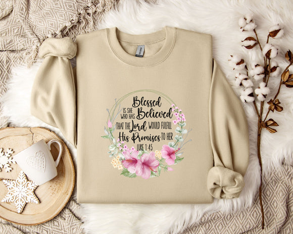 A beige sweatshirt with a floral design and text printed on it, along with a mug, a branch of cotton flowers, and a wooden tray.