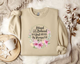 A beige sweatshirt with a floral design and text printed on it, along with a mug, a branch of cotton flowers, and a wooden tray.