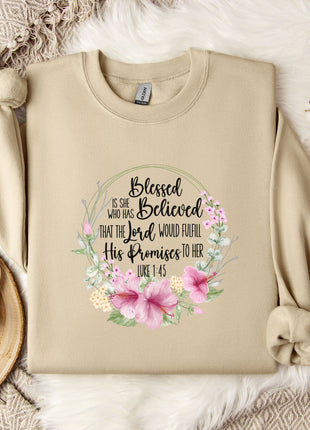 A beige sweatshirt with a floral design and text printed on it, along with a mug, a branch of cotton flowers, and a wooden tray.