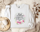 A white t-shirt with a floral design and text printed on it, placed on a bed with a white blanket and a mug.