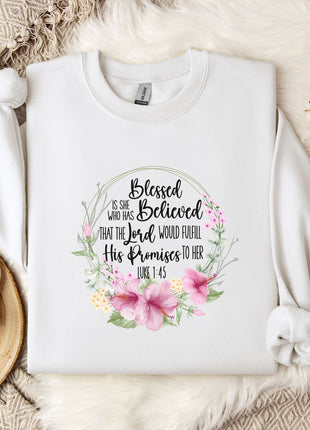 A white t-shirt with a floral design and text printed on it, placed on a bed with a white blanket and a mug.