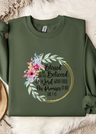 A green sweatshirt with a floral design and text printed on it, along with a mug and some white flowers on a bed.