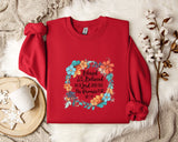 A red sweater with a floral design and text printed on it, along with a mug, a white mug, and some white flowers on a white fur rug.