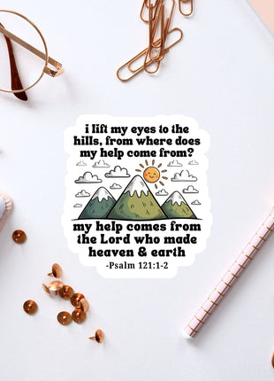 a sticker with a Bible verse and a mountain landscape, along with a pair of glasses, a pen, and some office supplies.
