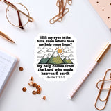 a sticker with a Bible verse and a mountain landscape, along with a pair of glasses, a pen, and some office supplies.