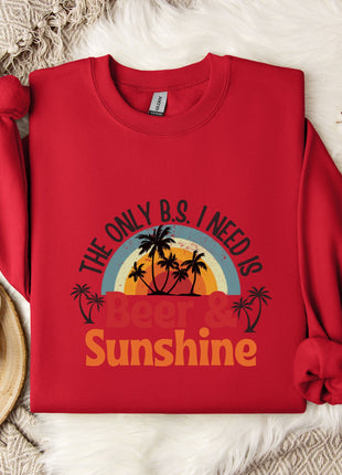 A red sweatshirt with a graphic design that says "The only B.S. I need is Beer & Sunshine" is displayed on a bed with a white blanket and a white mug.