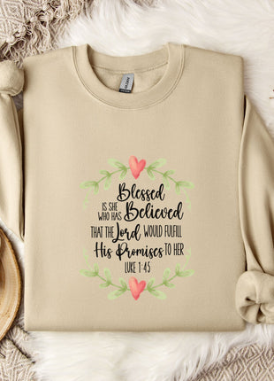 A beige sweatshirt with a printed Bible verse and a floral design, along with a mug, a white mug with a heart design, and some white cotton balls, all placed on a white fur rug.