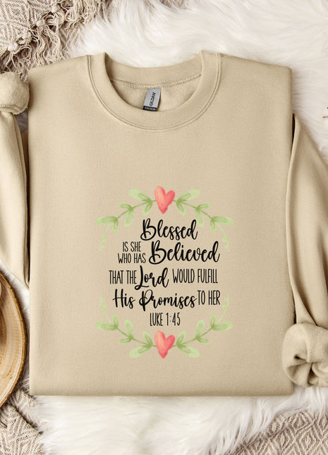 A beige sweatshirt with a printed Bible verse and a floral design, along with a mug, a white mug with a heart design, and some white cotton balls, all placed on a white fur rug.