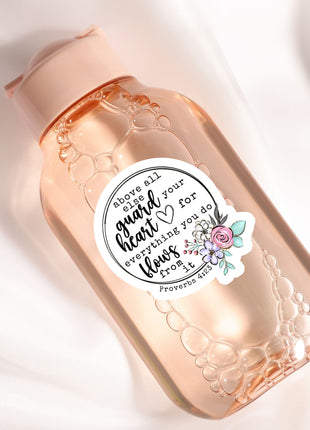 A pink bottle with a label that contains text and a floral design.