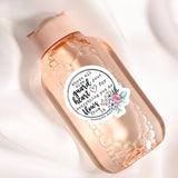 A pink bottle with a label that contains text and a floral design.