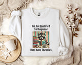 a white t-shirt with a graphic design of a raccoon reading a book, accompanied by the text "I'm Not Qualified To Diagnose" and "But I Have Theories".
