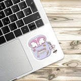 A sticker of a pair of pink earbuds with a cartoon character on a laptop keyboard.