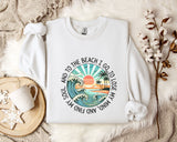 A white sweatshirt with a graphic design depicting a beach scene, along with the text "And to the beach I go, I lose my mind" printed on it. The sweatshirt is laid out on a bed with a floral patterned blanket, and there is a mug and a branch of cotton balls nearby.