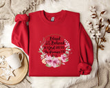 A red sweater with a floral design and text printed on it, placed on a white fur rug.