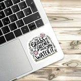 A sticker with a hand-drawn illustration of a watering can and the text "The grass is greener where you water it" is placed on the side of a laptop keyboard.
