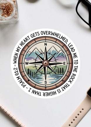 a compass with a mountain landscape and a quote around it, along with some office supplies and a pair of glasses on a white surface.