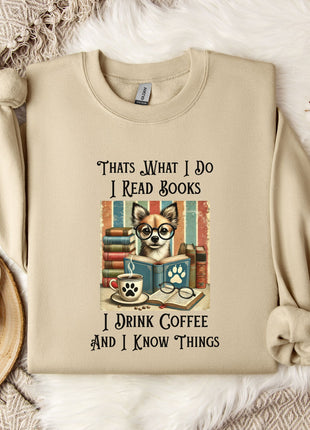 A beige sweatshirt with a printed design of a cat wearing glasses and surrounded by books, along with text that says "Thats What I Do I Read Books I Drink Coffee and I Know Things".