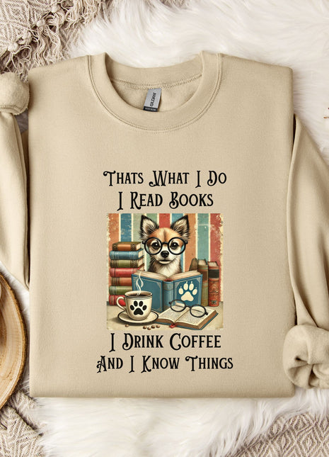 A beige sweatshirt with a printed design of a cat wearing glasses and surrounded by books, along with text that says "Thats What I Do I Read Books I Drink Coffee and I Know Things".