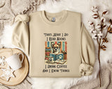 A beige sweatshirt with a printed design of a cat wearing glasses and surrounded by books, along with text that says "Thats What I Do I Read Books I Drink Coffee and I Know Things".