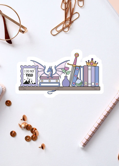 a sticker with a dragon and various objects, such as books, a pen, and a pair of glasses, arranged on a white surface.