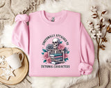 A pink sweatshirt with a graphic design of a skeleton surrounded by flowers and books, along with the text "Emotionally Attached to Fictional Characters".