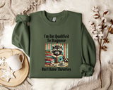 a green sweatshirt with a graphic design of a raccoon reading a book, accompanied by the text "I'm Not Qualified To Diagnose But I Have Theories".