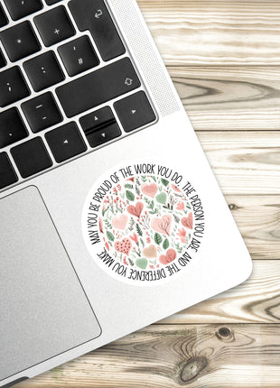 A sticker with a floral design is placed on the edge of a laptop keyboard, resting on a wooden surface.