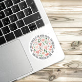 A sticker with a floral design is placed on the edge of a laptop keyboard, resting on a wooden surface.
