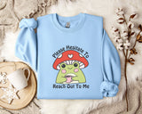 A light blue sweatshirt with a mushroom graphic and text, along with a mug and some white flowers, all laid out on a white fur rug.