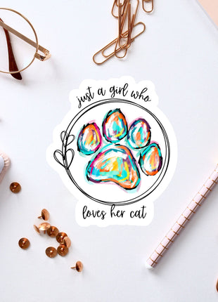 a sticker with a paw print and the text "Just a girl who loves her cat" surrounded by various office supplies such as pens, a notebook, and a pair of glasses.
