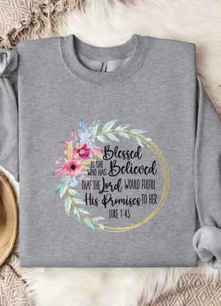 A gray sweatshirt with a floral design and text printed on it, along with a mug and some cotton balls on a bed with a blanket.