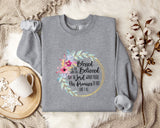 A gray sweatshirt with a floral design and text printed on it, along with a mug and some cotton balls on a bed with a blanket.