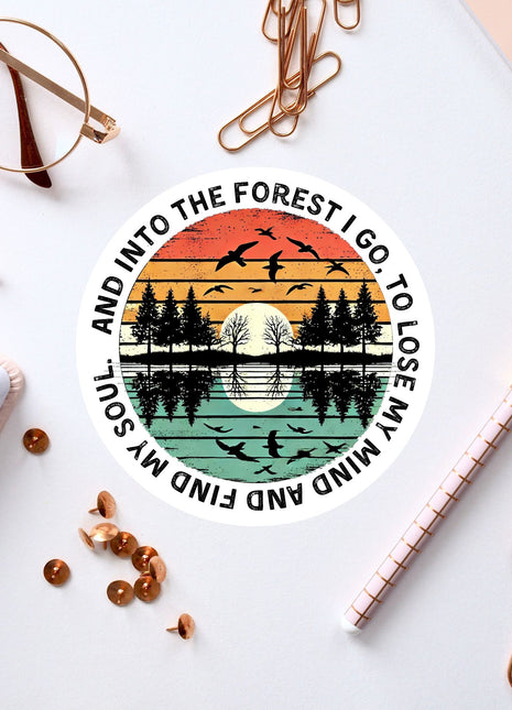 a circular sticker with a sunset and trees design, surrounded by various office supplies such as pens, a notebook, and a pair of glasses.