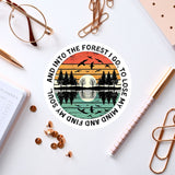 a circular sticker with a sunset and trees design, surrounded by various office supplies such as pens, a notebook, and a pair of glasses.