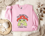A pink sweatshirt with a cartoon frog wearing a red mushroom hat and holding a cup, accompanied by a mug, a branch of cotton bolls, and a text that says "Per My Last Email I Hate You".