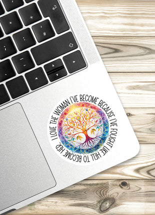 A sticker with a colorful tree design is placed on the edge of a laptop keyboard.