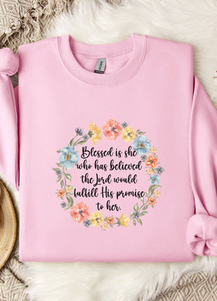 A pink sweatshirt with a floral wreath design and a quote printed on it, placed on a white fur rug.