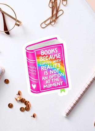 a sticker with a book and a quote, surrounded by various office supplies such as pens, a notebook, and a pair of glasses.