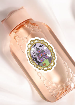 A pink bottle with a label featuring a castle and bats, along with a decorative border.