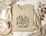 A beige sweatshirt with a floral design and text printed on it, along with a mug, a branch of cotton bolls, and a snowflake.